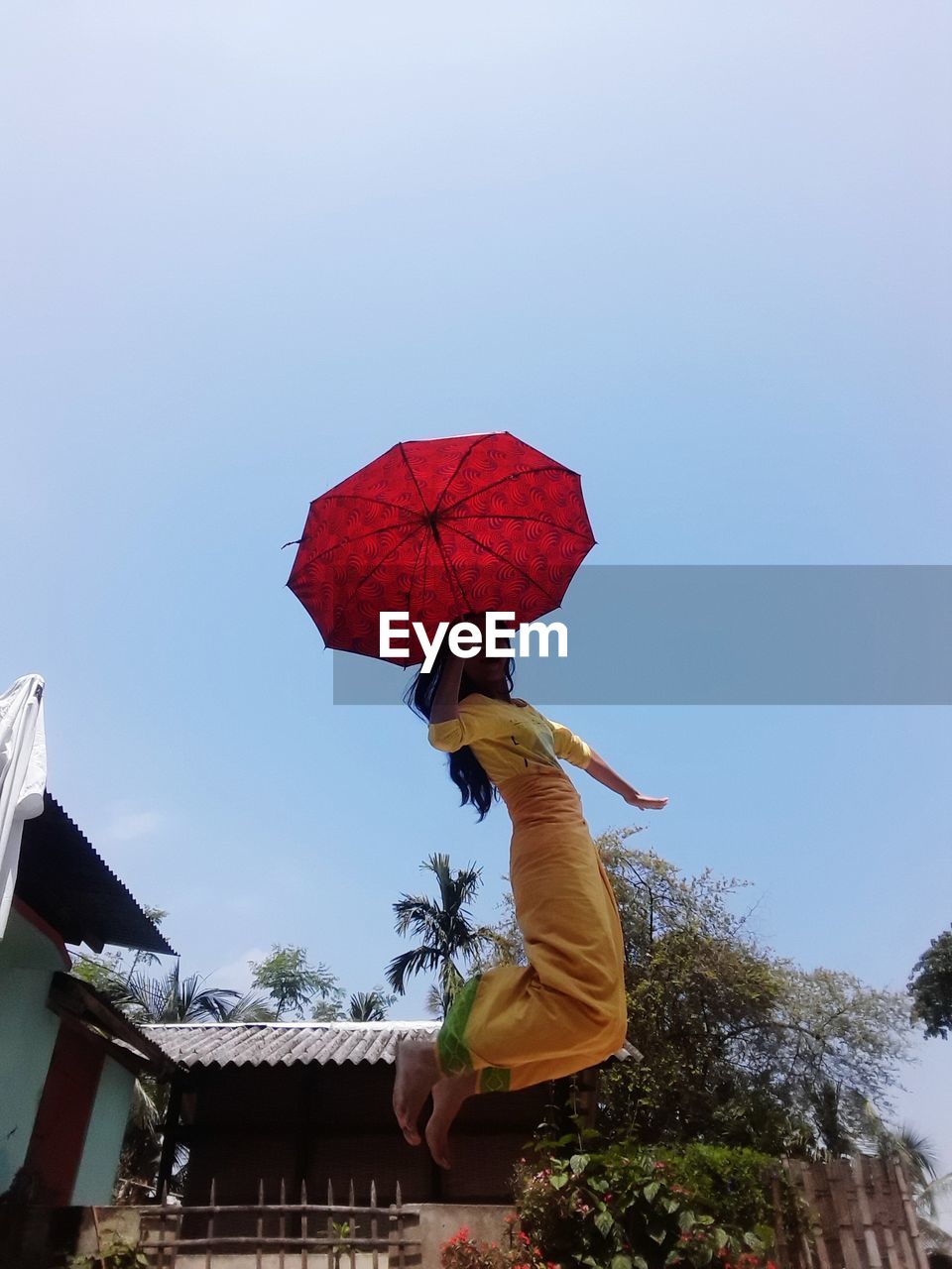 LOW ANGLE VIEW OF WOMAN HOLDING UMBRELLA AGAINST CLEAR BLUE SKY