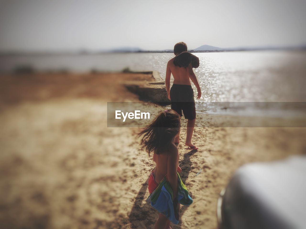 Shirtless siblings standing at beach against sky