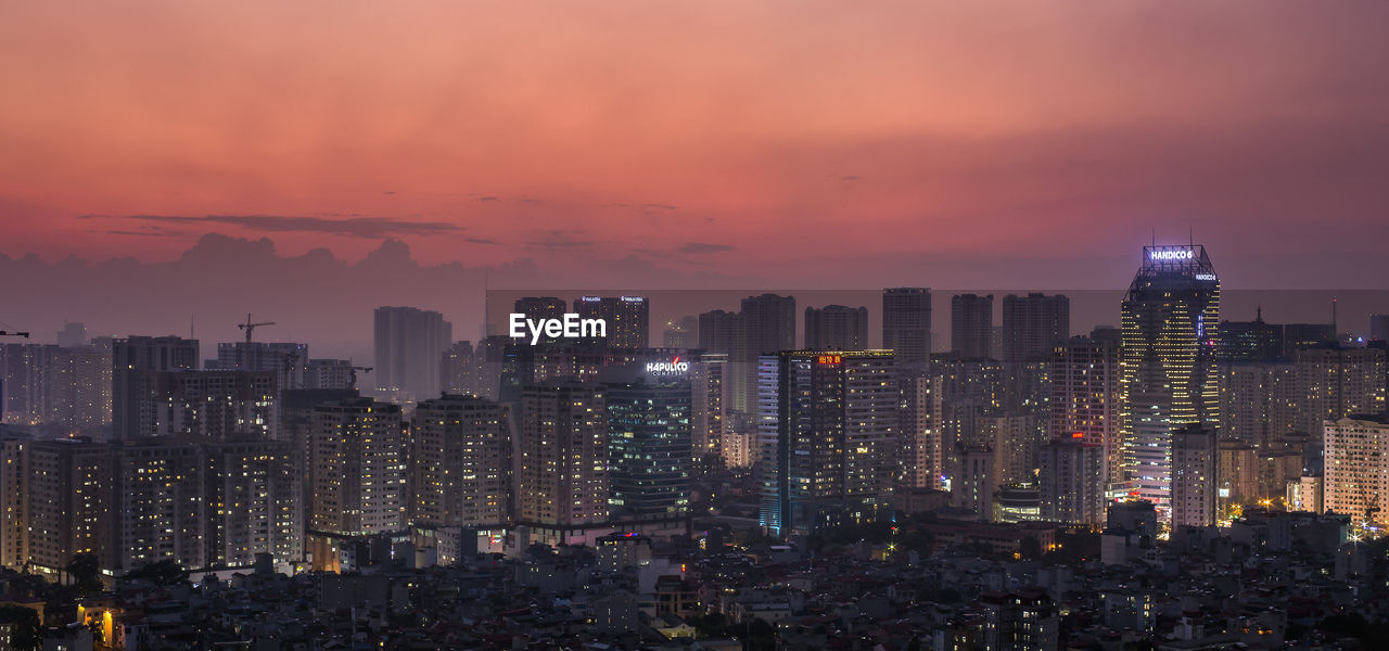 Illuminated buildings in city against sky during sunset