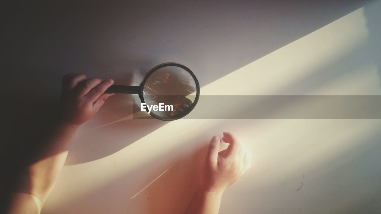 Cropped hands of child holding magnifying glass against wall