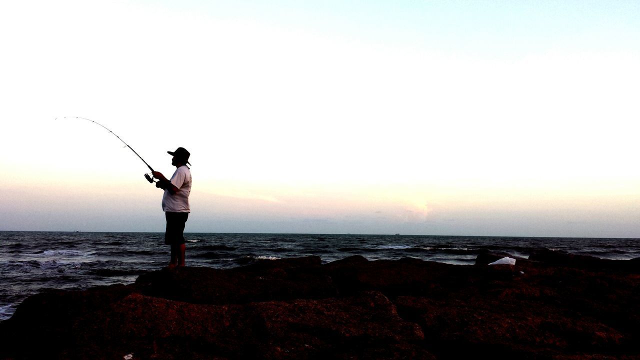 Man with fishing rod standing on rocks at shore