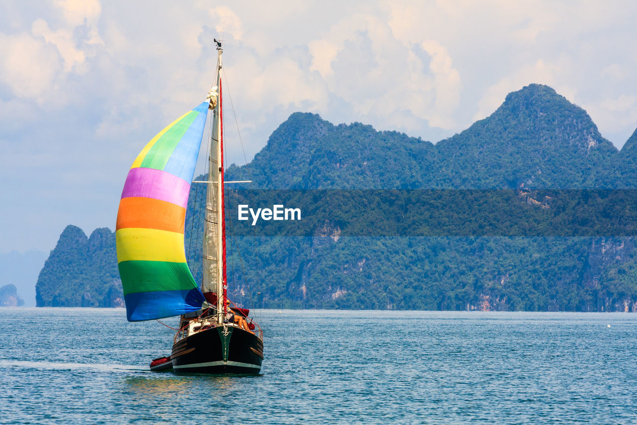 VIEW OF SAILBOAT IN SEA AGAINST MOUNTAIN