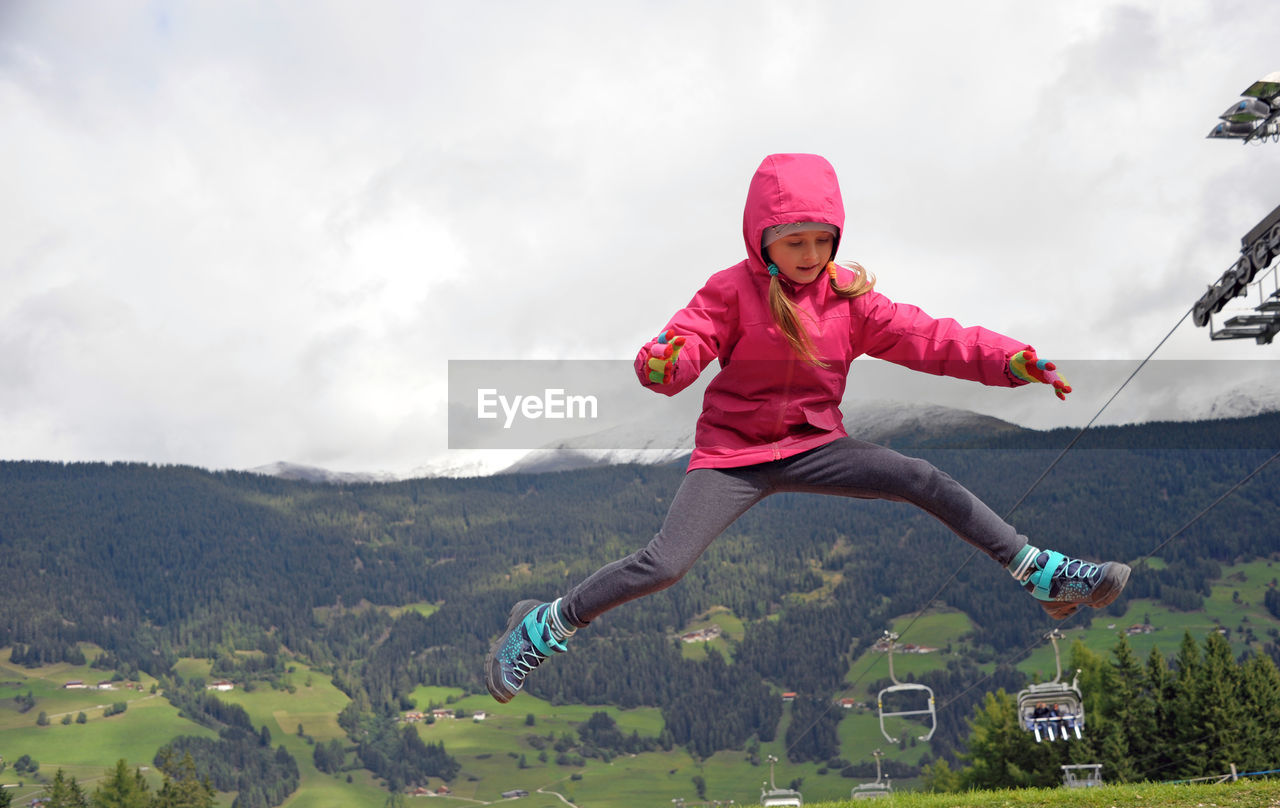 Full length of girl jumping against mountains and sky