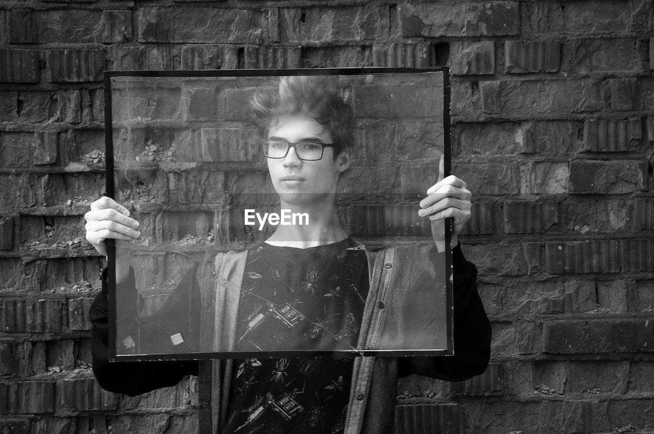 Teenage boy holding glass frame while standing against wall