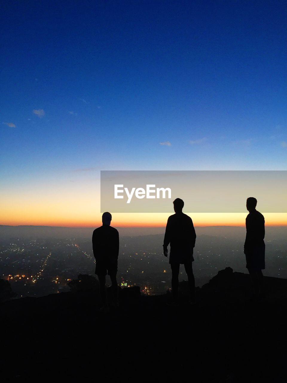 Silhouettes of three young man looking at cityscape at dusk