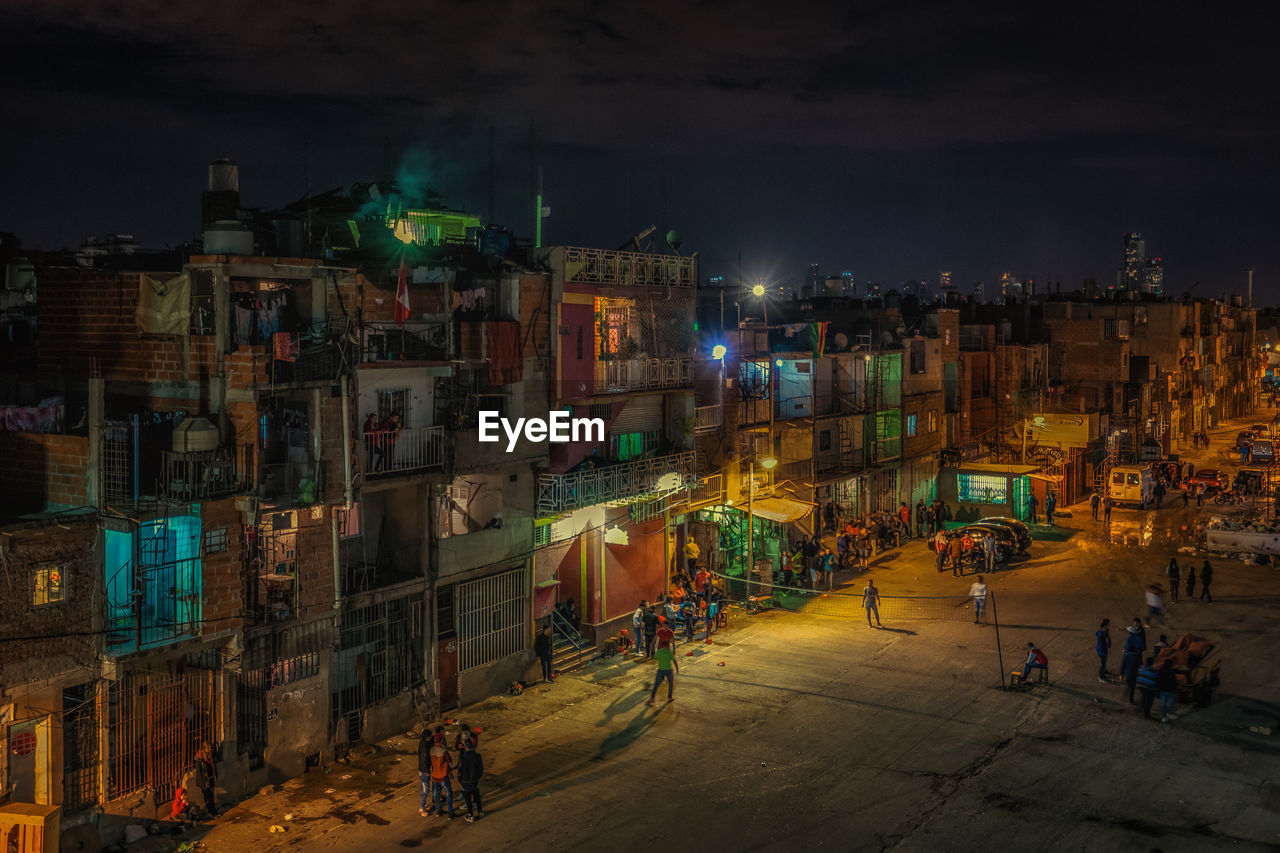 High angle view of people on road by residential buildings against sky at night