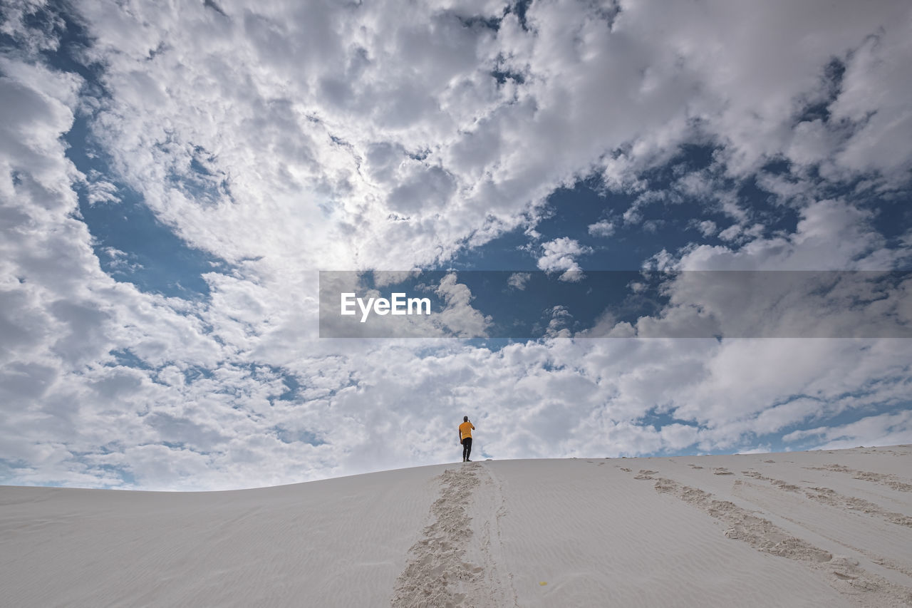 Rear view of man standing on sand in desert against sky