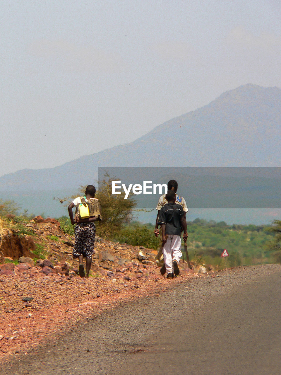 REAR VIEW OF MEN WALKING ON ROAD AGAINST MOUNTAINS