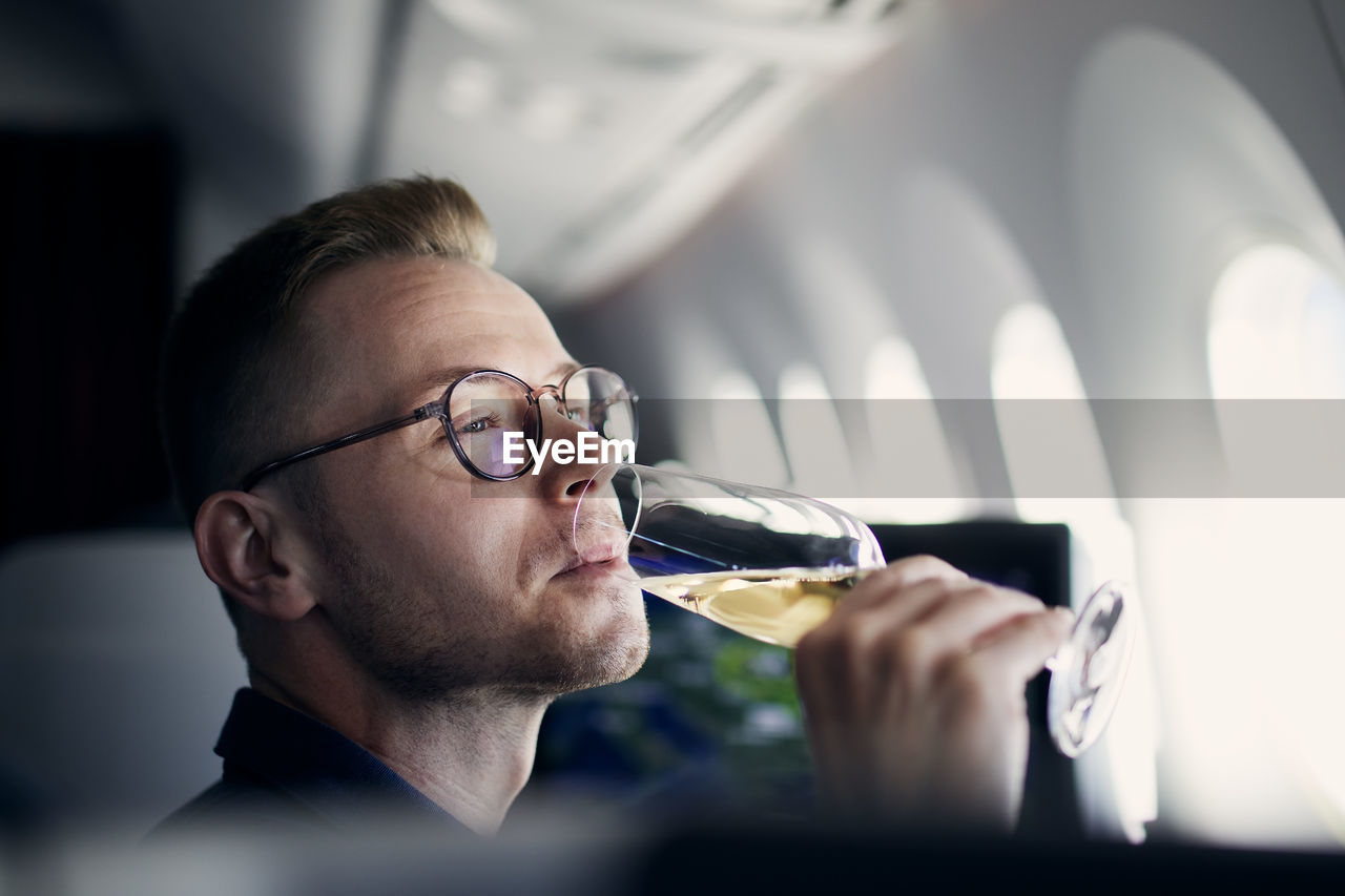Business travel by airplane. man looking through window and drinking champagne during flight.