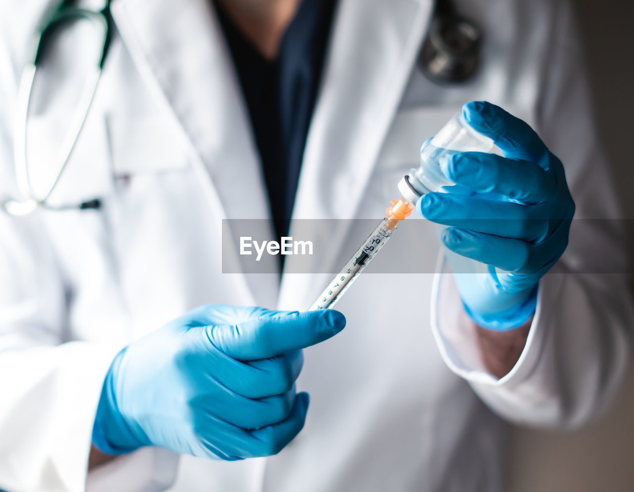 Doctor in white coat drawing vaccine into a syringe for injection.