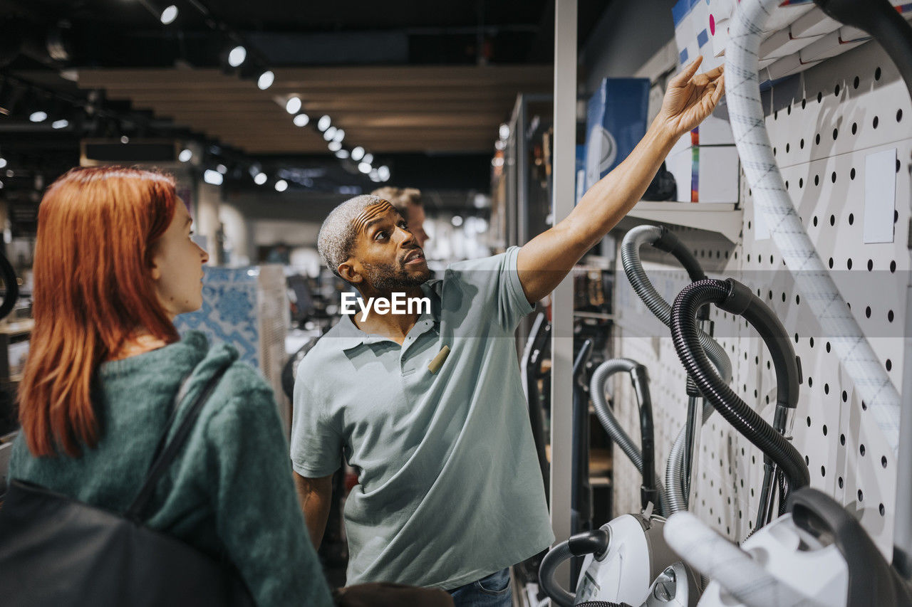 Salesman advising female customer in buying modern appliance at electronics store