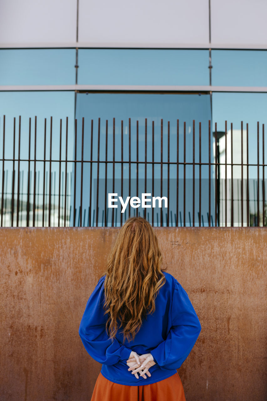 Rear view of woman standing with hands behind back while facing wall