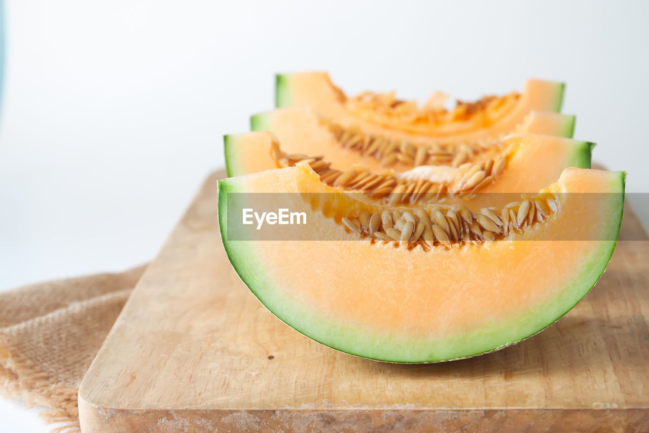 Close-up of cantaloupe slices on cutting board against white background