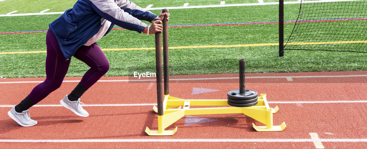 A high school girl is pushing a yellow sled with seventy five pounds of weight down a red track.