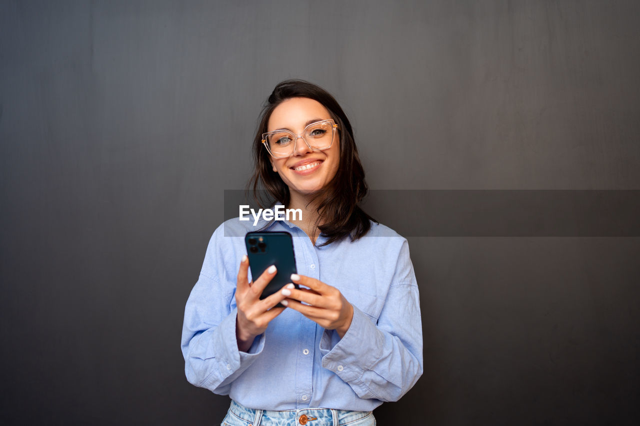 young woman using mobile phone against wall