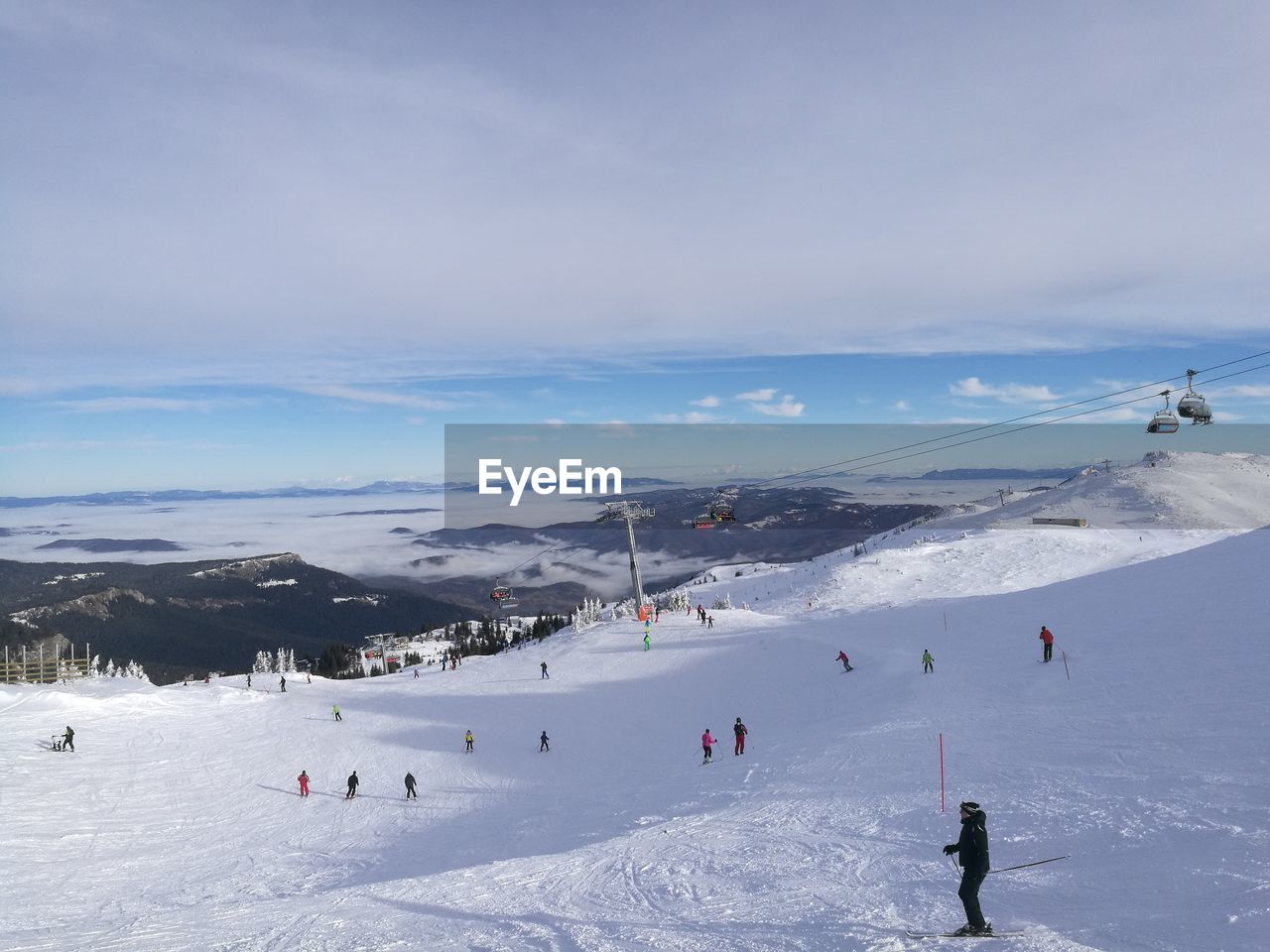 People skiing on snow covered mountain against cloudy sky