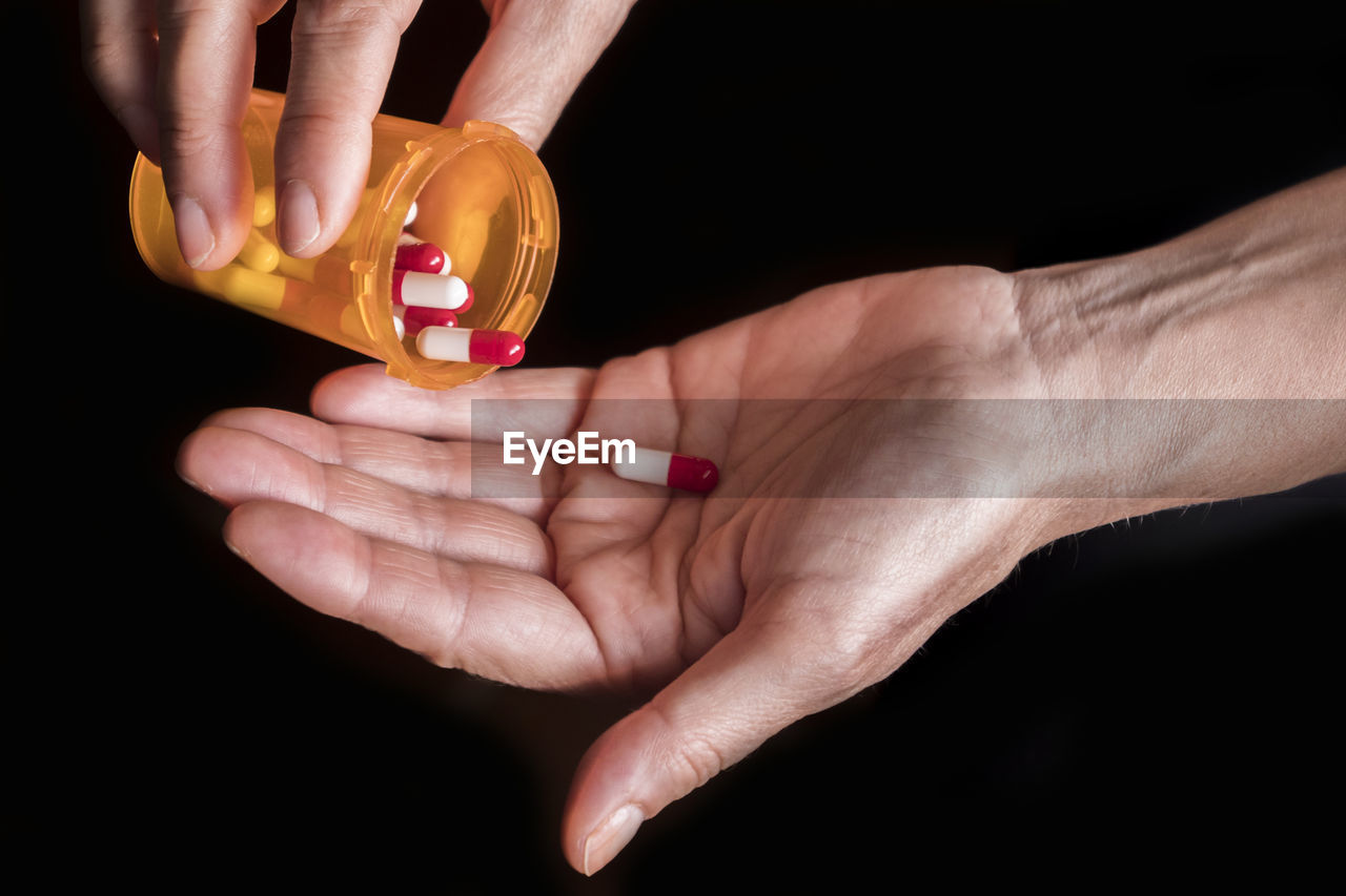 Close-up of hands holding capsules over black background