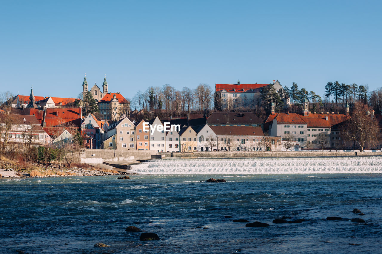 Buildings by river against clear blue sky