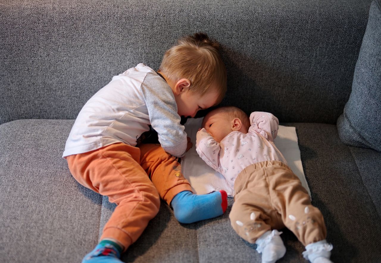 Cute little toddler and his newborn baby sister on the sofa