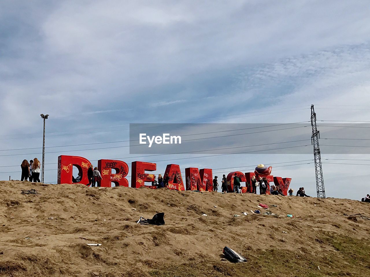 People walking by text on landscape against cloudy sky