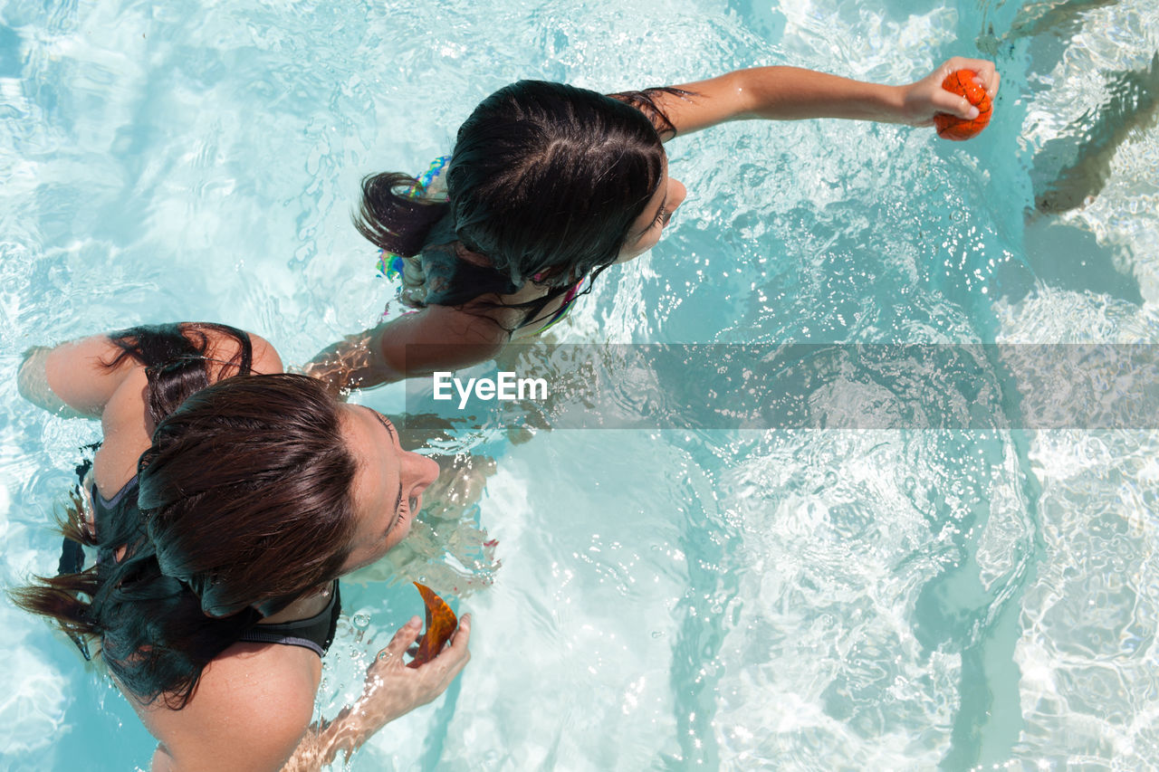 Directly above shot of smiling woman with daughter enjoying in swimming pool