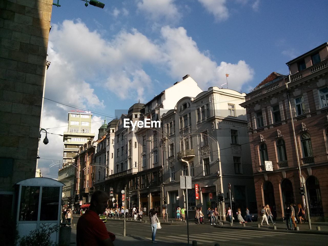 People at city street amidst buildings against cloudy sky