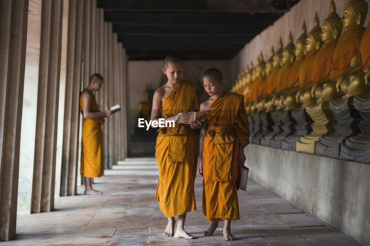 Monks reading book while walking in corridor