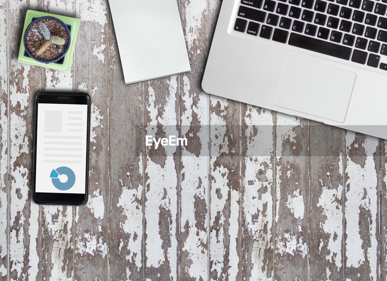 Directly above shot of laptop with mobile phone by note pad and plant on wooden table