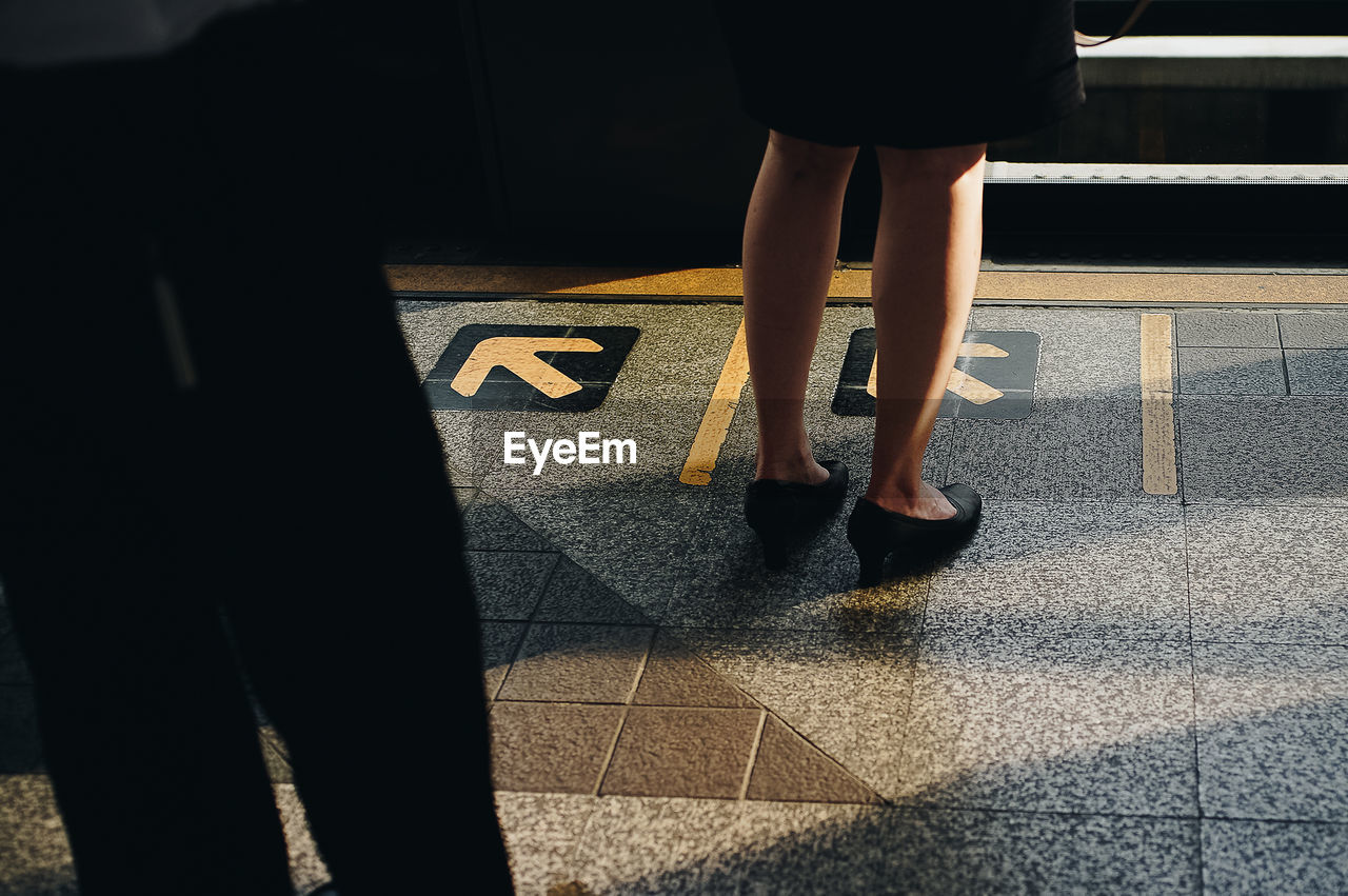 Low section of woman standing at railroad station platform