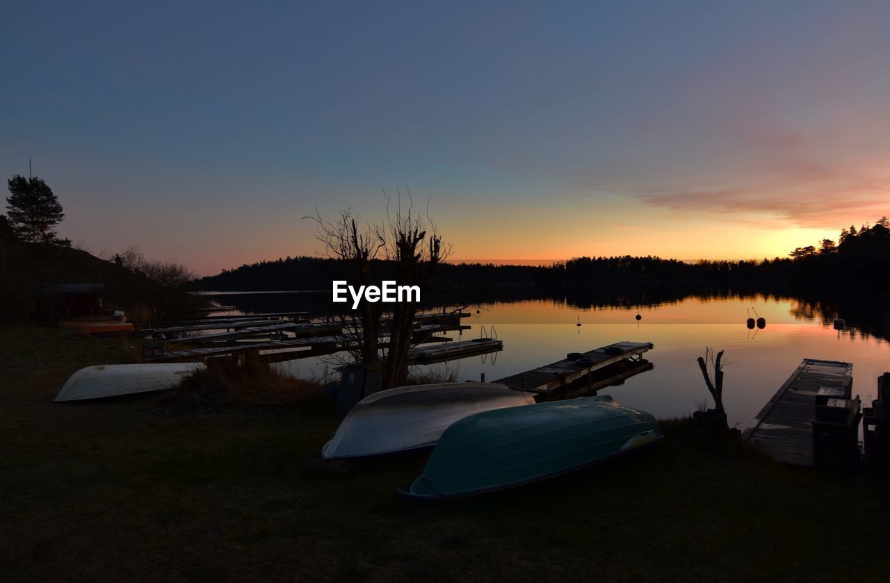 Boats moored in lake against sky during sunset