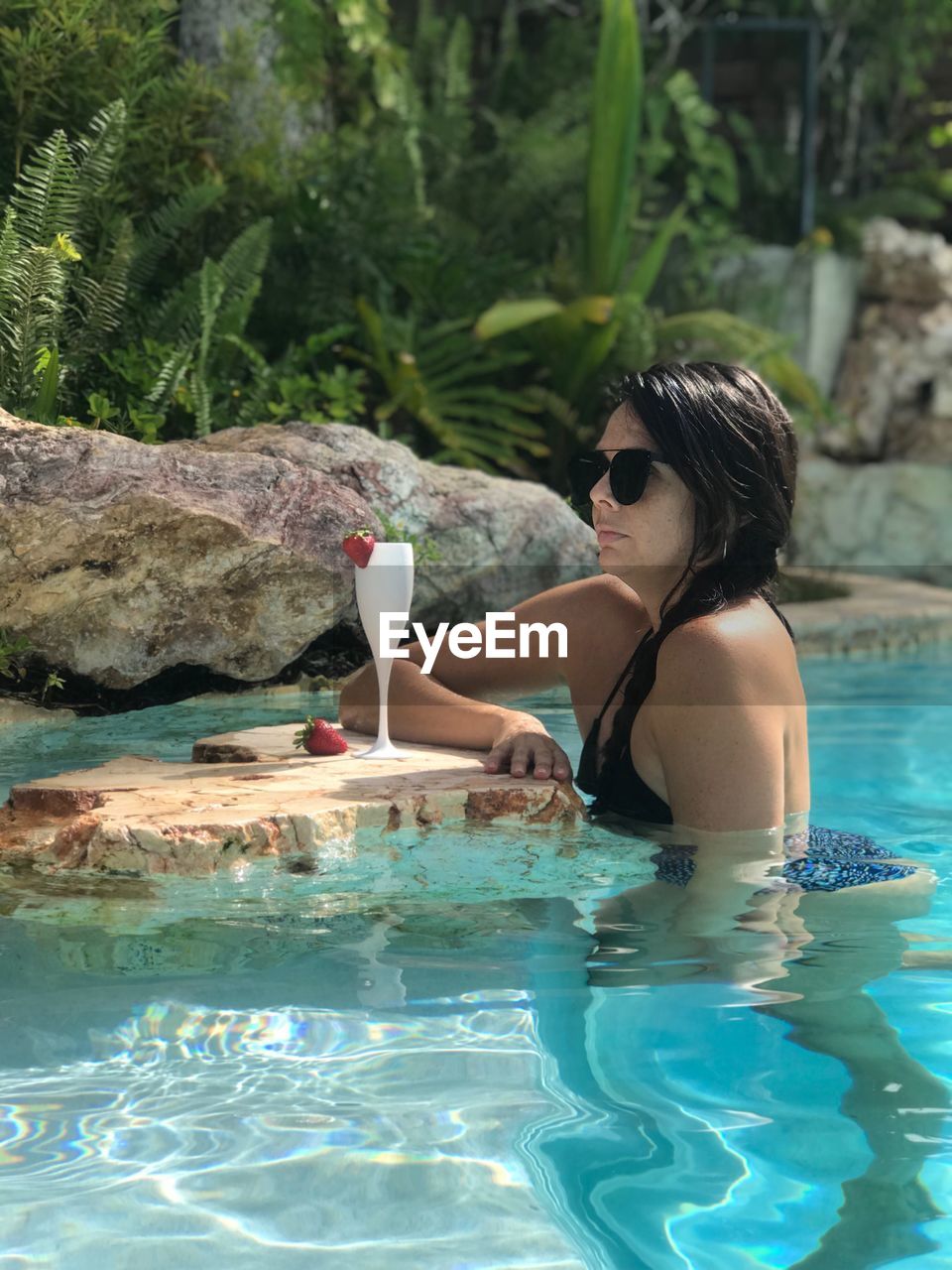 Side view of mid adult woman wearing sunglasses swimming in pool