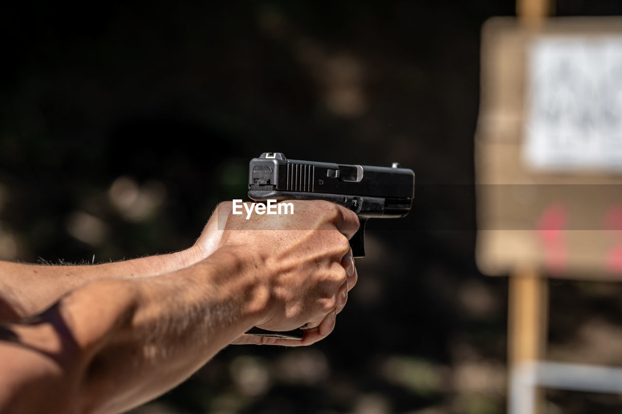 cropped hand of person holding gun against black background