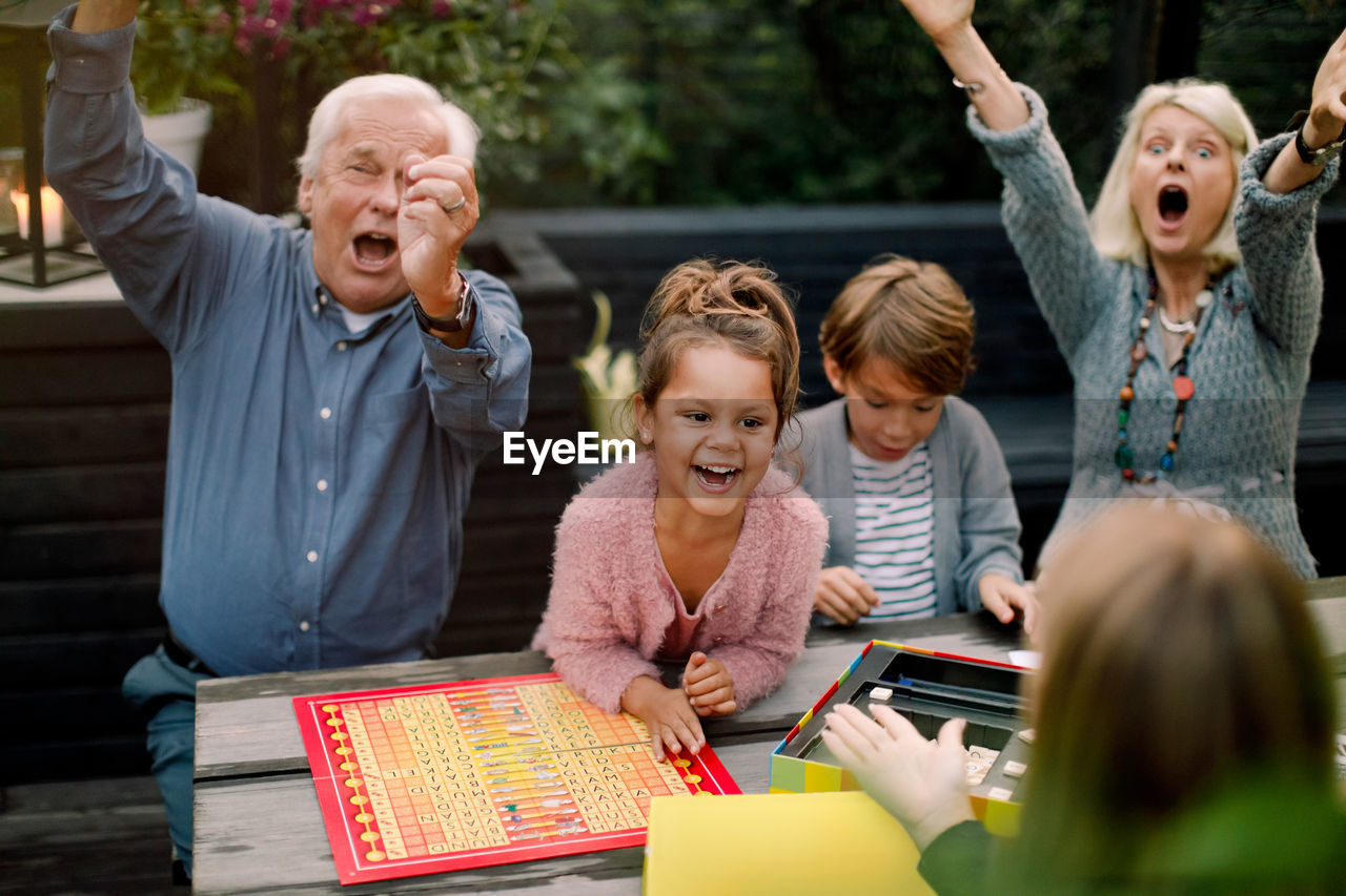 Smiling cheerful family playing board game while sitting at table in backyard