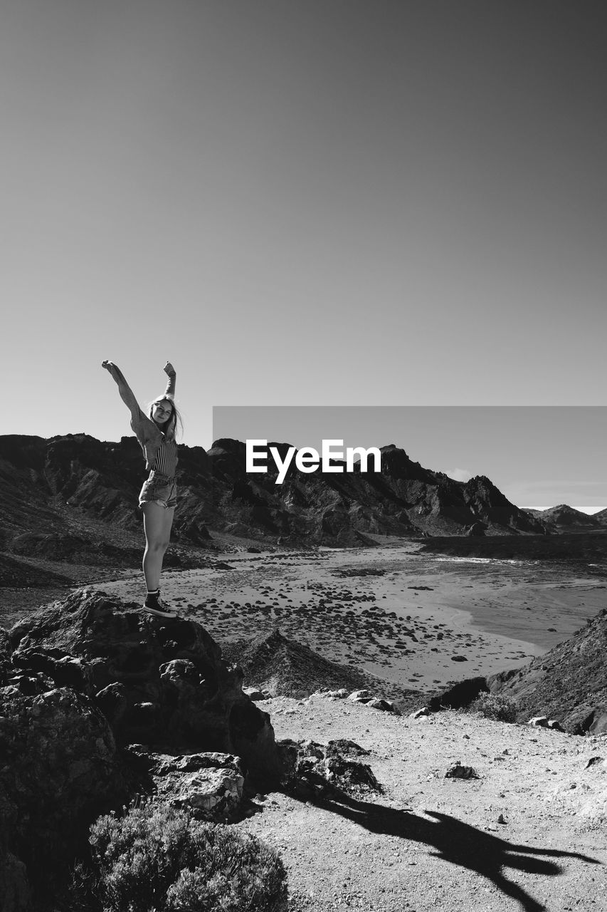 YOUNG WOMAN STANDING AT BEACH AGAINST CLEAR SKY