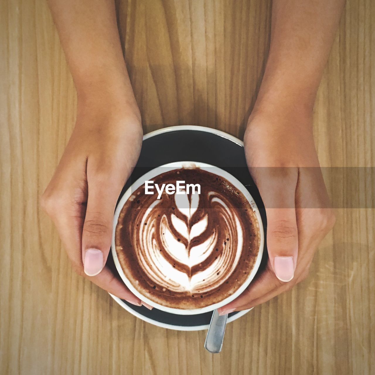 Cropped image of woman holding coffee cup on wooden table