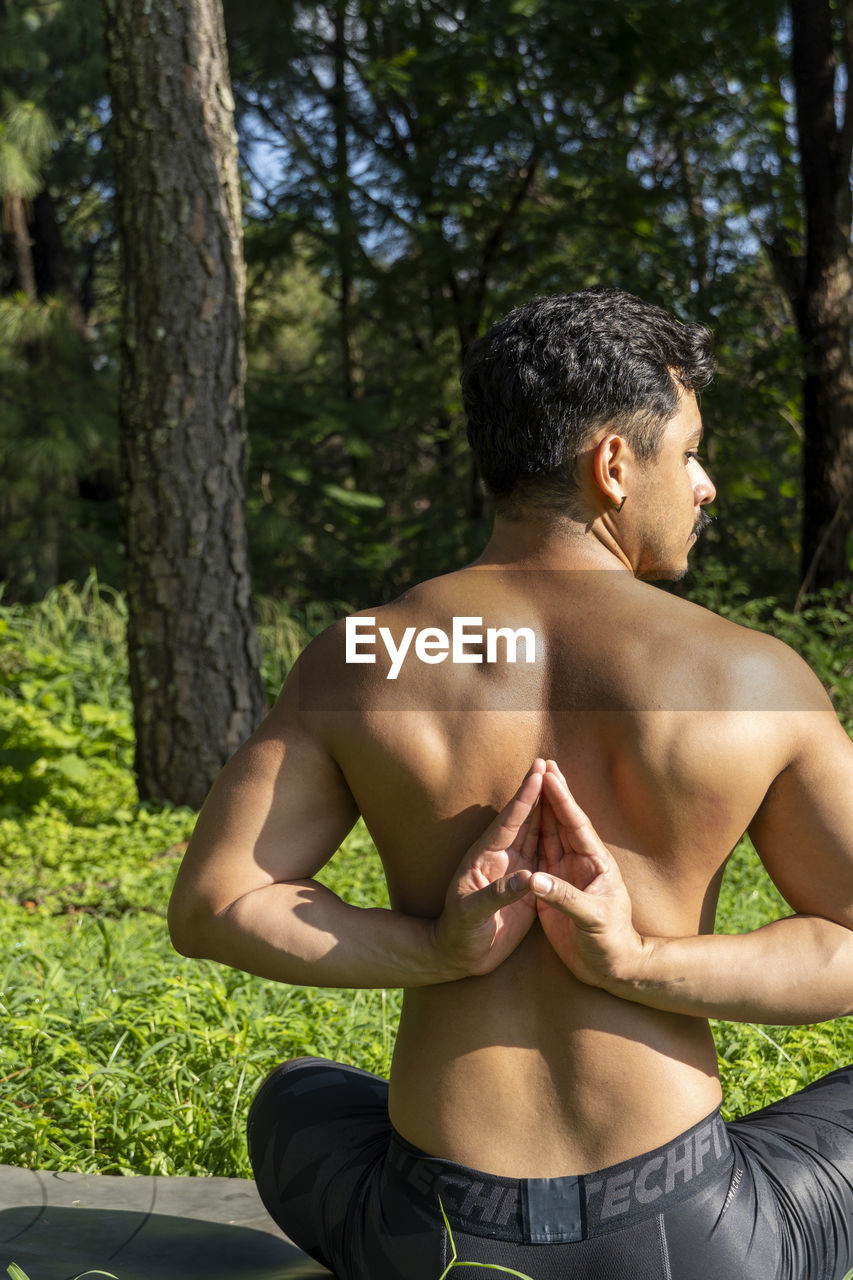 Latin american man doing yoga posture, yoga posture, bee backwards prsthatah brahmara, forest