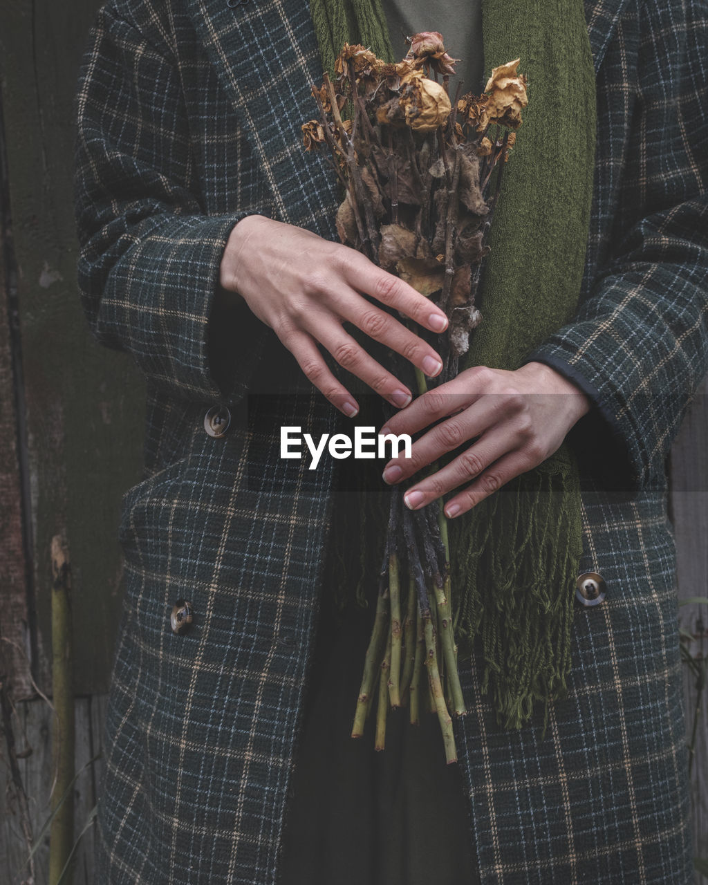 A woman in a green warm coat holds a dried bouquet of roses in her hands. monochrome tones.