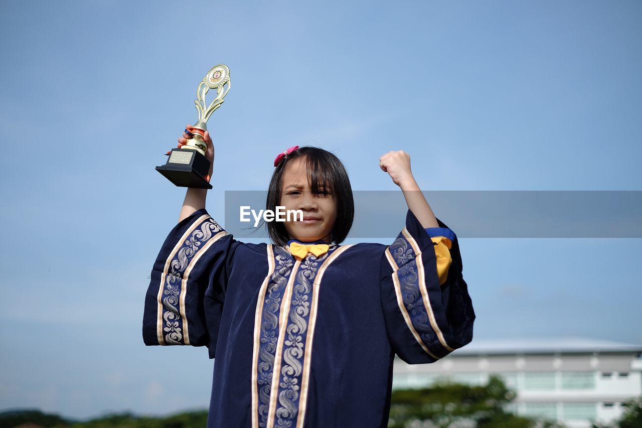 Portrait of confident girl with trophy against sky