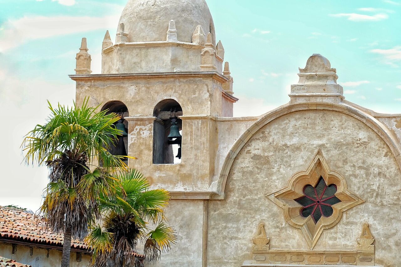 High section of bell tower by palm trees against sky