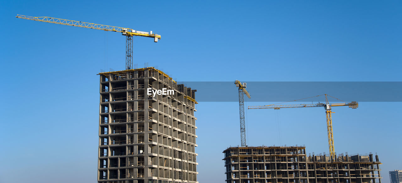 LOW ANGLE VIEW OF CRANE AND BUILDINGS AGAINST CLEAR SKY