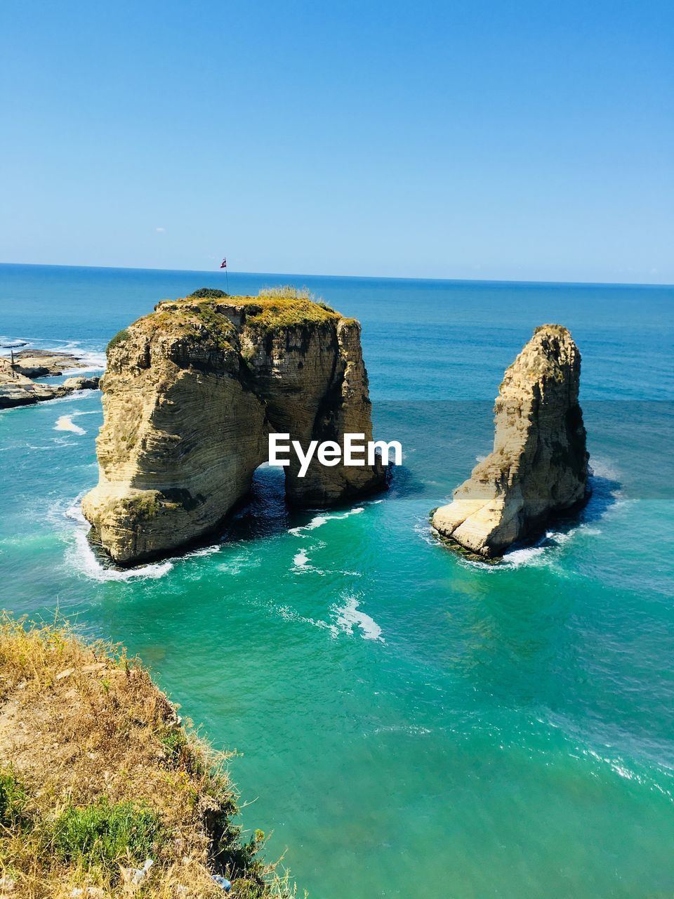 Rocks in sea against clear blue sky