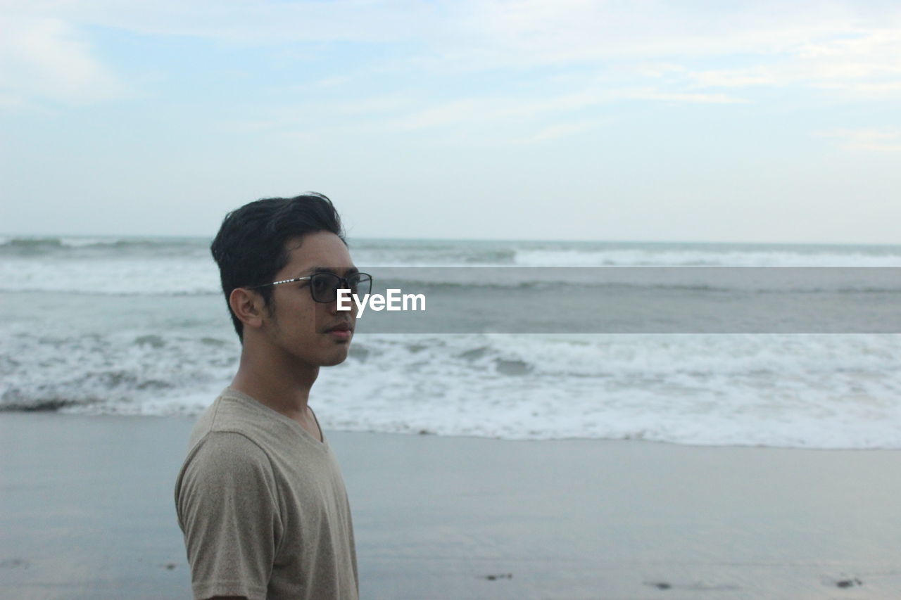 Young man looking away while standing on beach