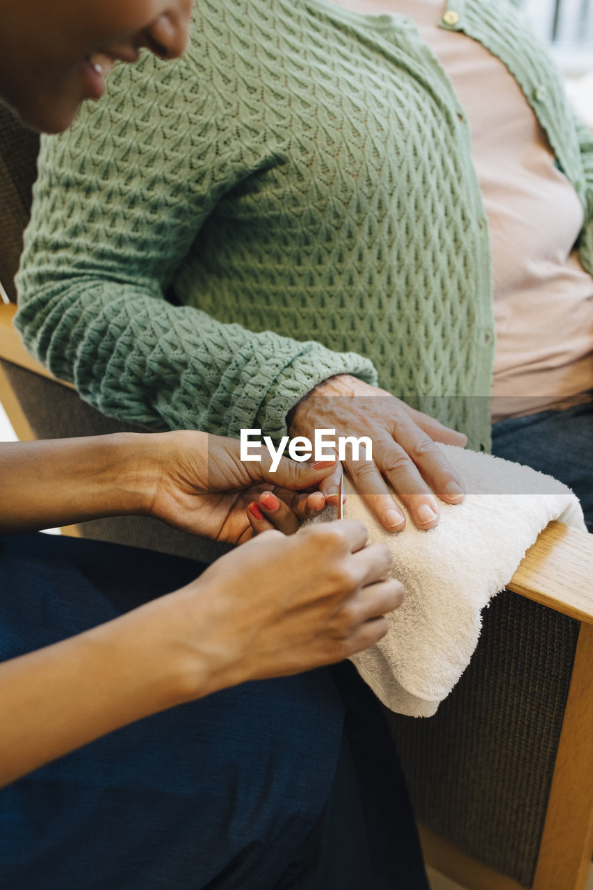 Midsection of senior woman getting her nails in shape from young female caretaker at nursing home