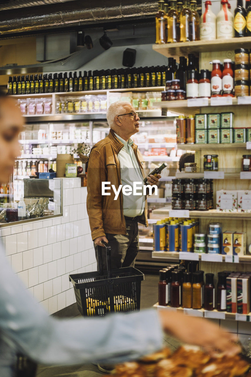 Senior man holding basket and bottle shopping at convenience store