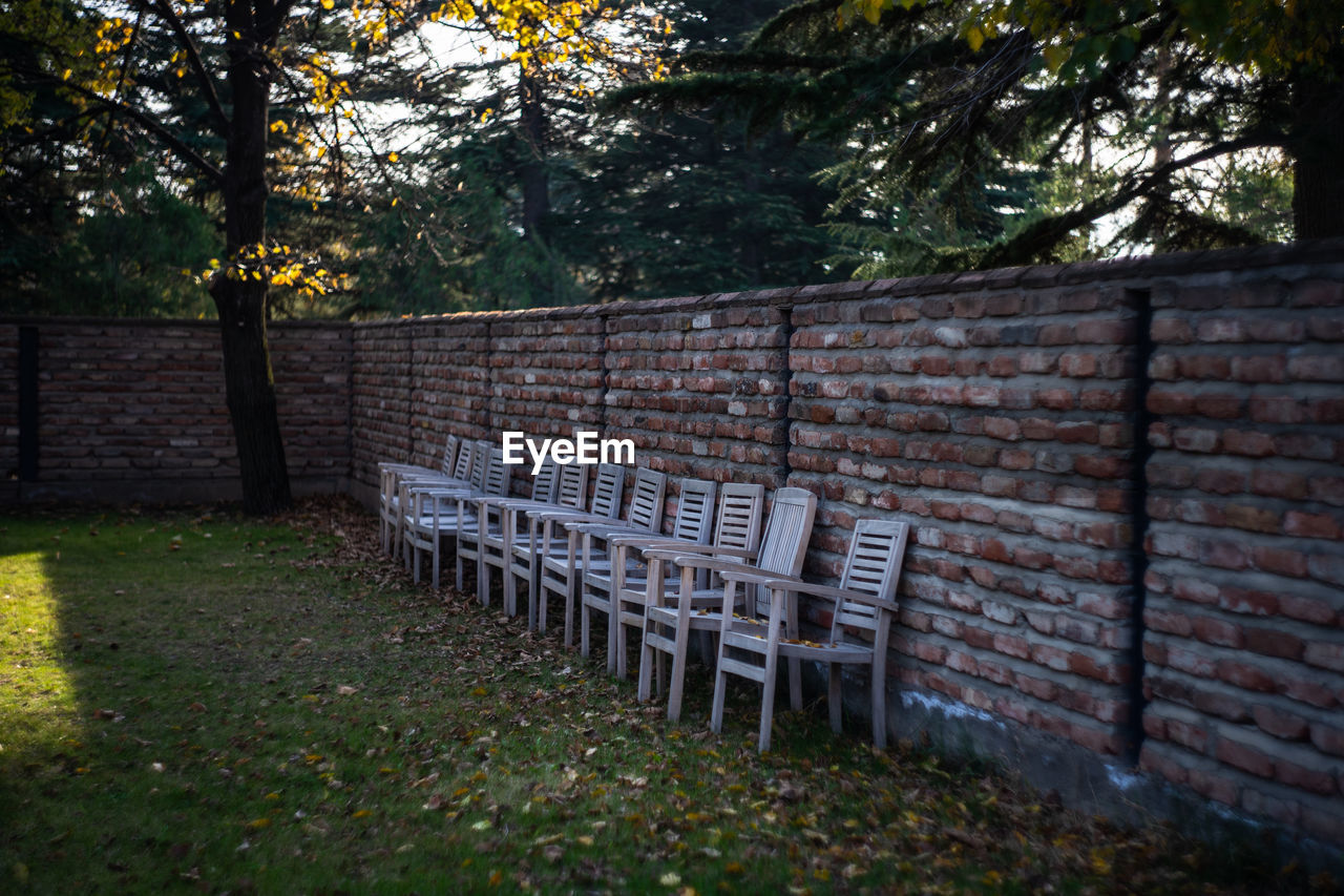 EMPTY PARK BENCH BY STONE WALL IN SUNLIGHT