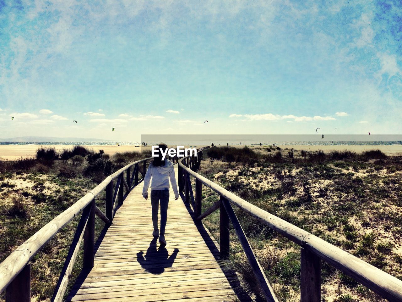 Rear view of woman walking on boardwalk against sky