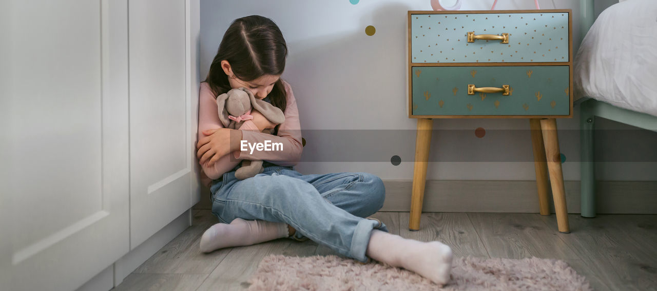 Sad girl hugging stuffed toy sitting on the floor