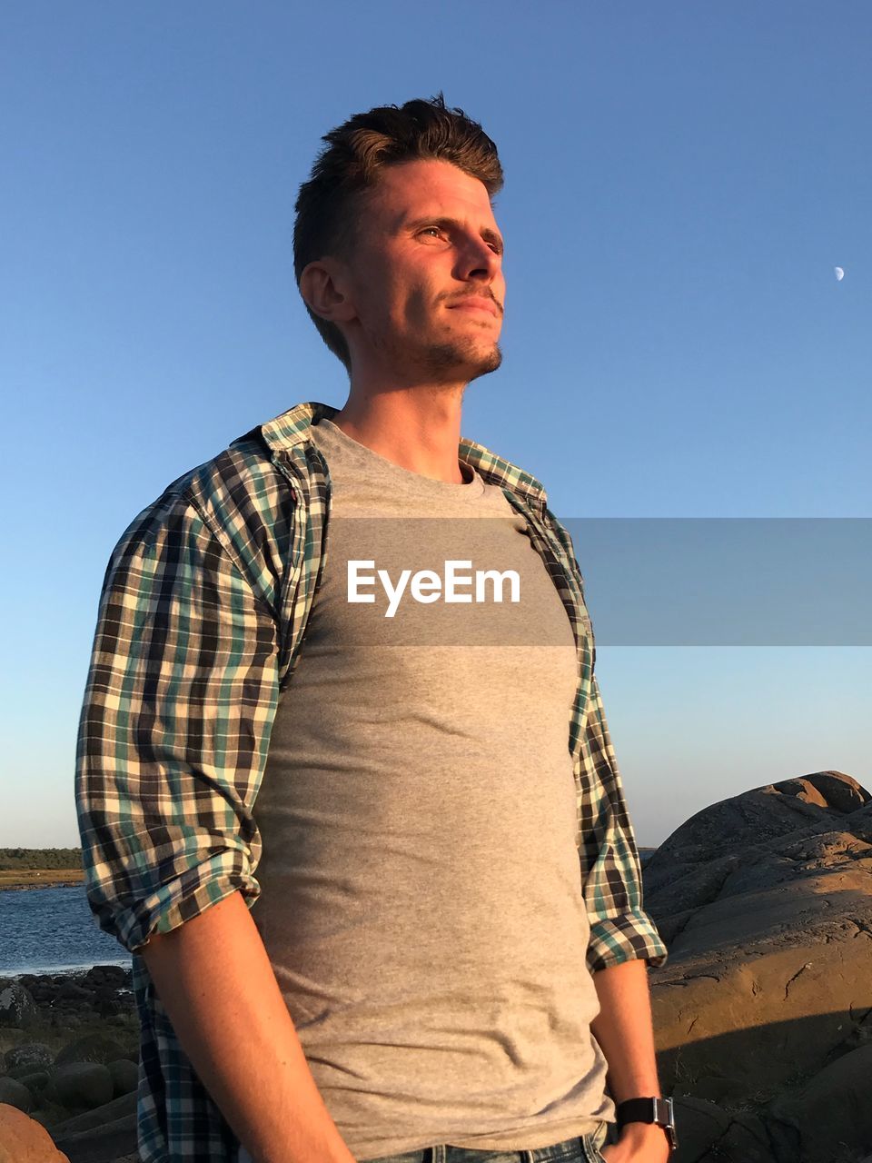 YOUNG MAN LOOKING AWAY AGAINST CLEAR SKY