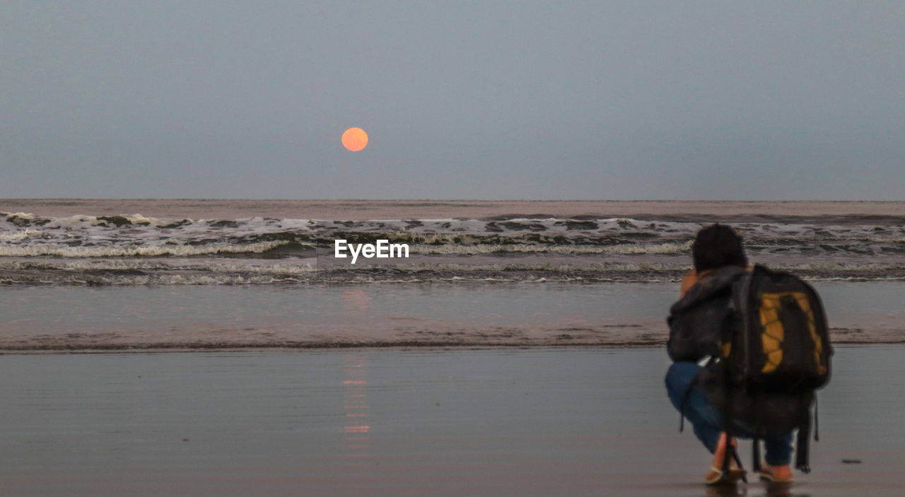 REAR VIEW OF WOMAN STANDING ON BEACH AGAINST SKY