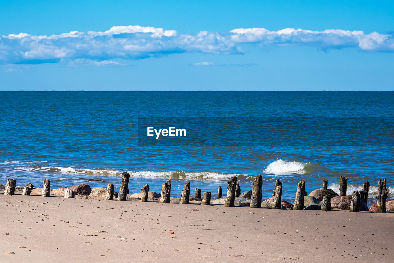 PANORAMIC VIEW OF WOODEN POSTS ON BEACH AGAINST SKY